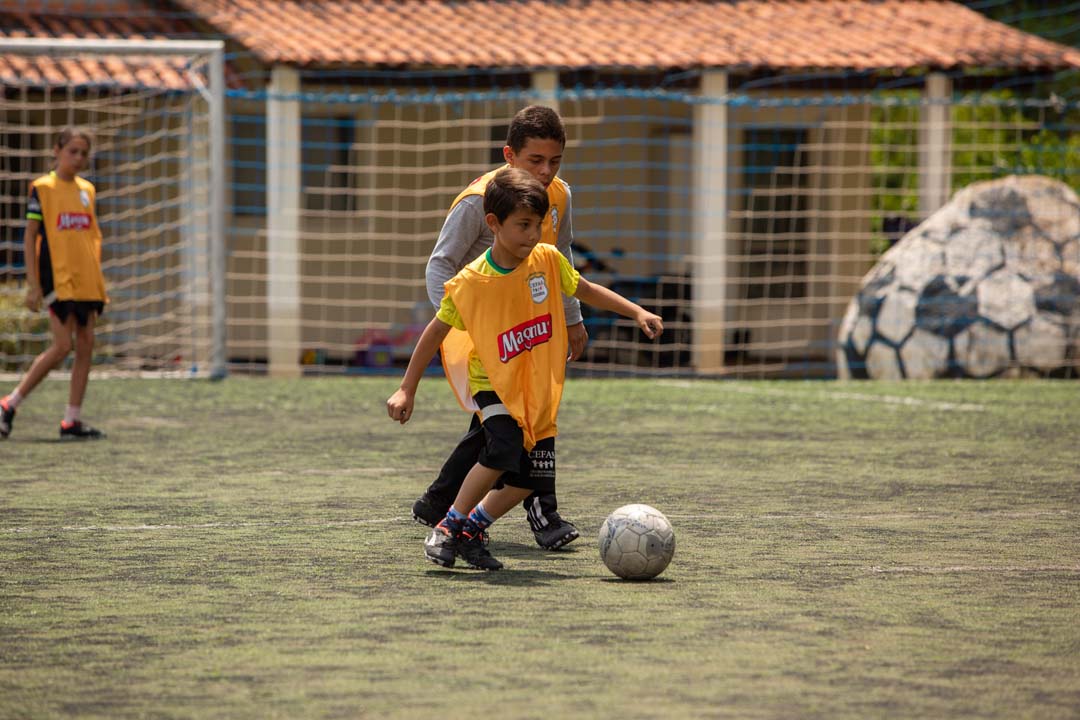Imagem de menino chutando a bola de futebol no campo durante atividade.