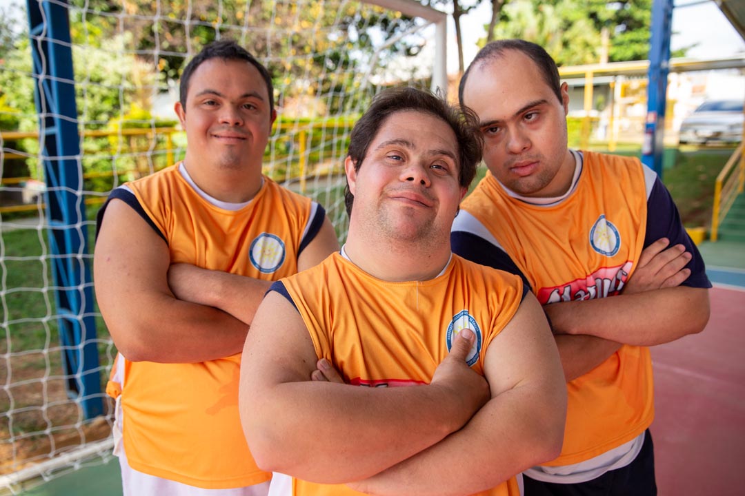 Na imagem 3 atletas do futsal down com os braços cruzados olhando para foto