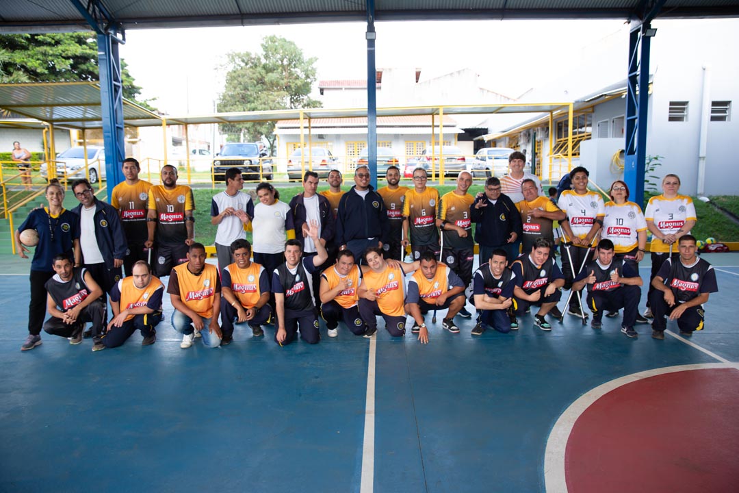 Na imagem atletas do Futsal down, Futsal de deficiência intelectual, atletas do vôlei sentado e dois professores olham para câmera e vestem uniforme da Magnus