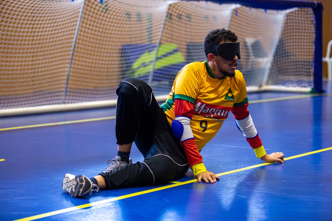 Na imagem atleta do Goalball sentado no chão com os olhos vendados, vestindo uniforme da Magnus