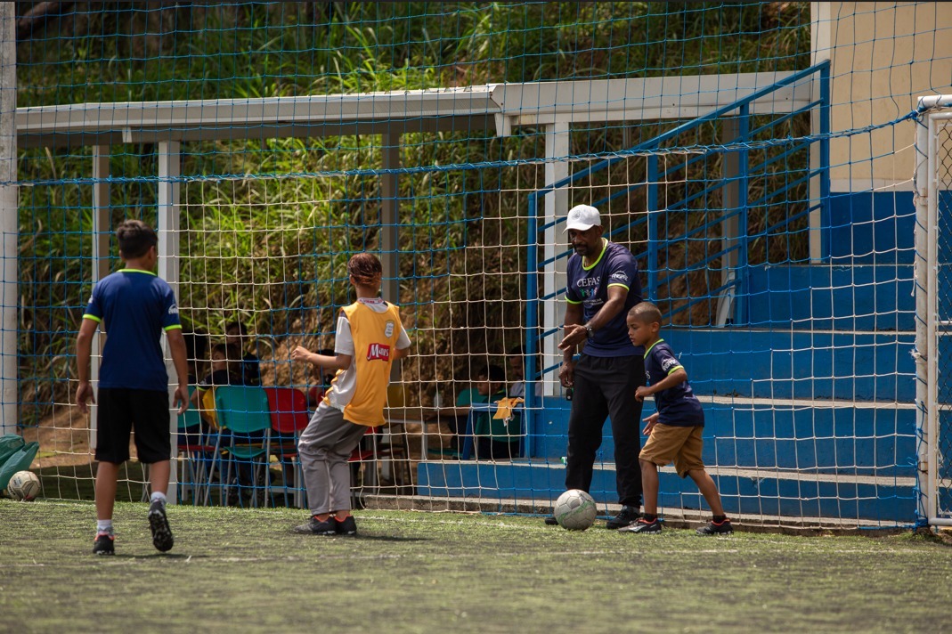 Na imagem o professor da organização assistencial CEFAS orientando 3 crianças em um campo de futebol
