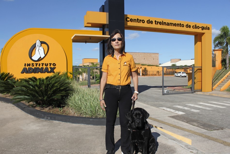 Na imagem Kátia Garcia com seu cão-guia Willy em frente ao centro de treinamento do Instituto Adimax