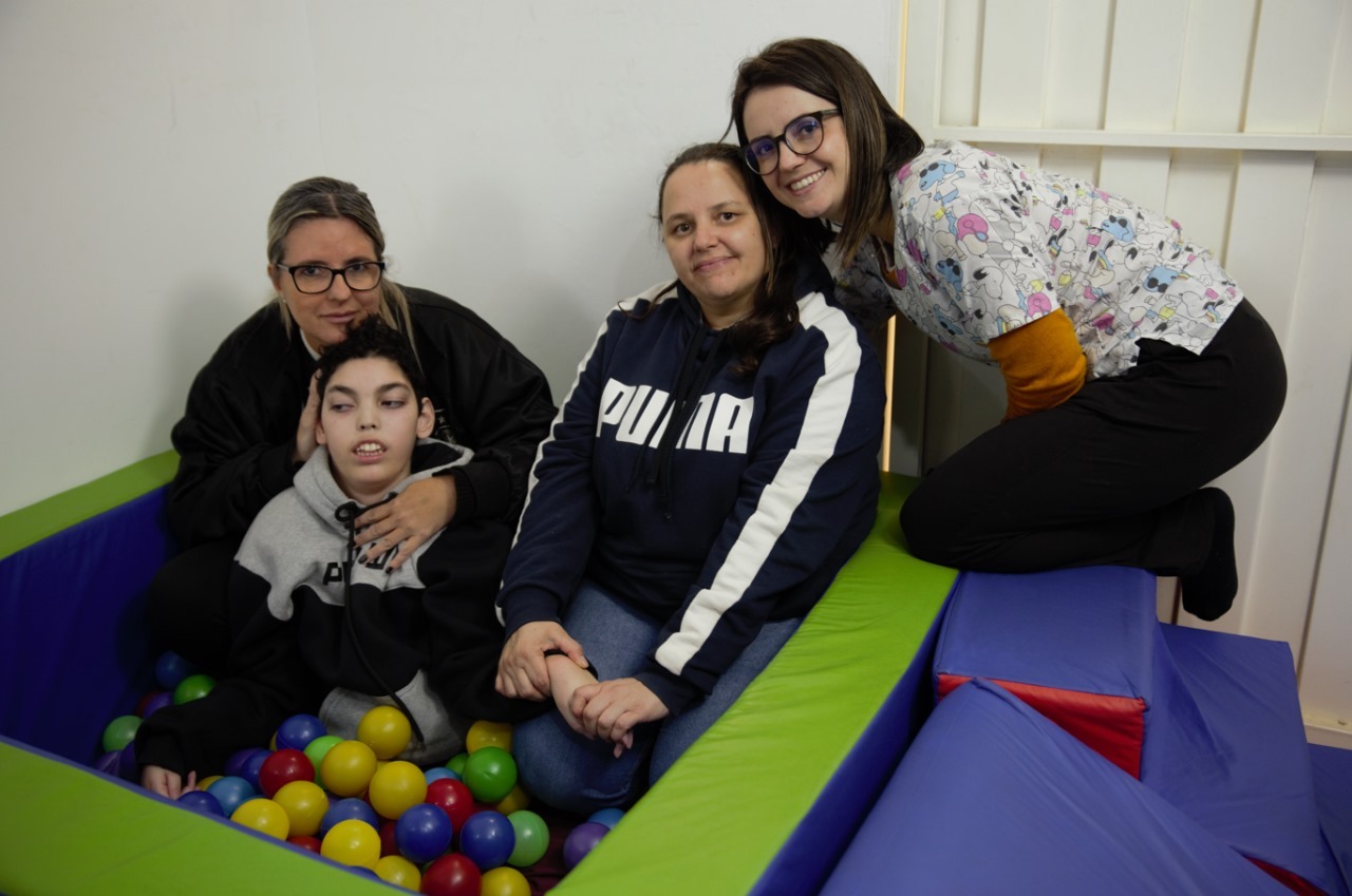 Na imagem três mulheres e uma criança neurodivergente posam para foto na sala sensorial